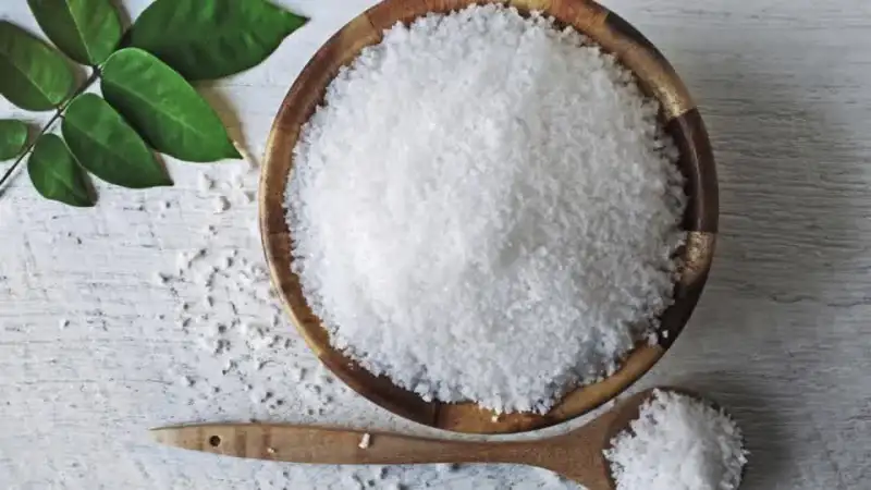 Wooden bowl and spoon with salt and green leaves