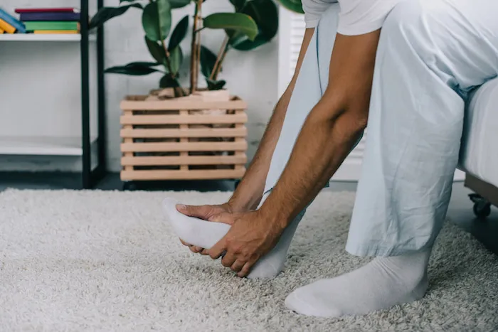 Man getting out of bed and holding foot in pain. | 7 Tips to Lower Uric Acid