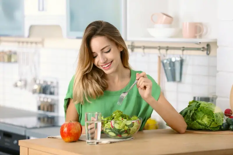 Woman eating salad at the kitchen table.