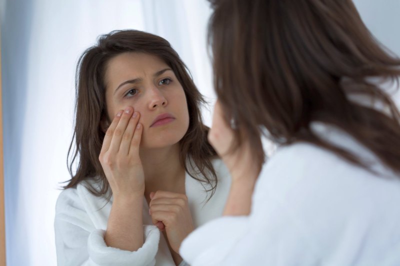 Woman touching her face while looking in the mirror.